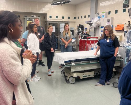  Students gather in circle around gurney in hospital room as medical personnel presents.